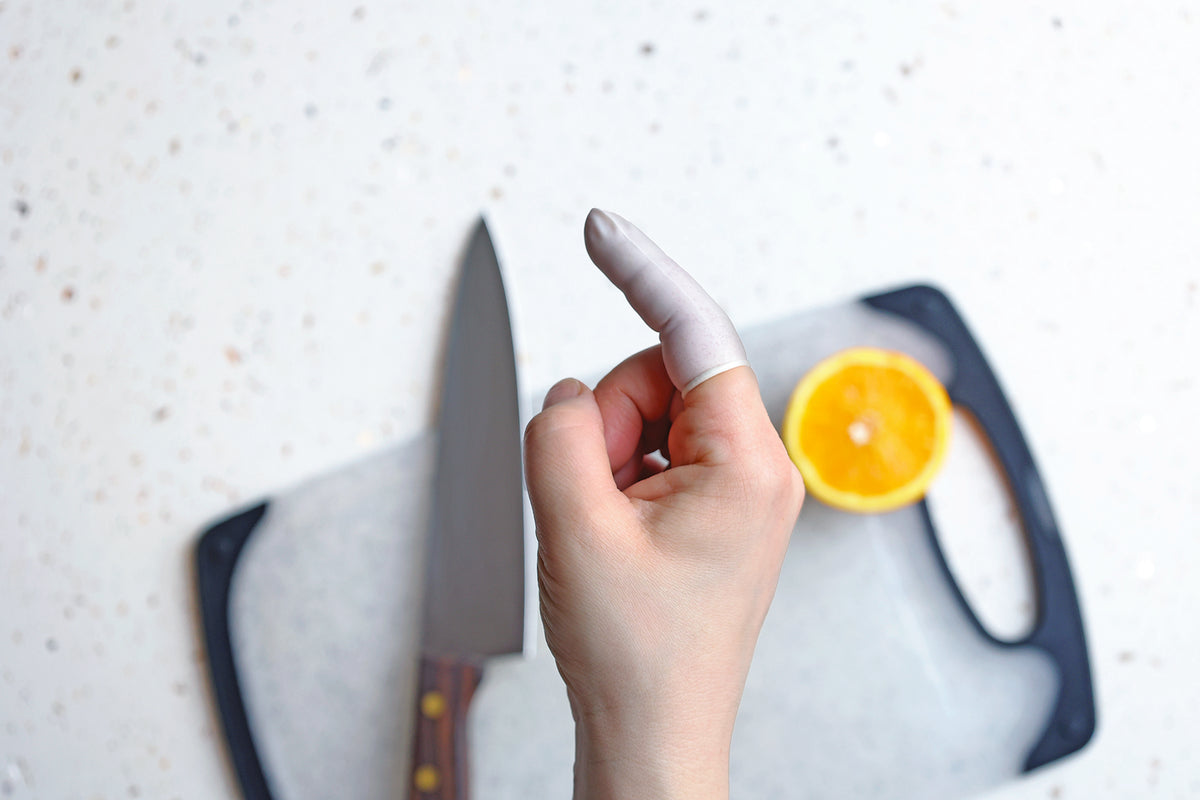 a hand with one finger wearing a finger cot with a knife and a cutting board on the background